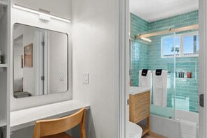 Un bagno con un mobile lavabo bianco, uno specchio, una sedia in legno e una zona doccia con piastrelle blu.