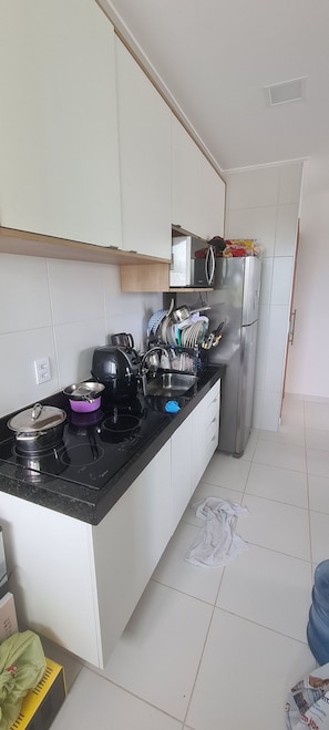 A kitchen with white cabinets, a black countertop, and a stainless steel refrigerator. - Mana Beach Experience (Ipojuca)