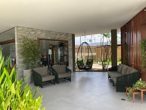 A modern outdoor seating area with wicker furniture, a hanging chair, and potted plants. - Mana Beach Experience (Ipojuca)