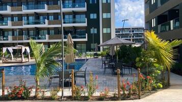 Un hotel moderno con piscina, mobiliario exterior y un jardín bien cuidado.