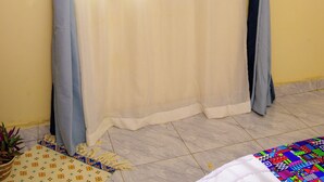 A room with a bed, a window with curtains, and a plant on the floor.