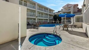 A swimming pool with lounge chairs and umbrellas, surrounded by multi-story buildings with balconies. - Howard Johnson By Wyndham Tempe University/Phoenix (Tempe)