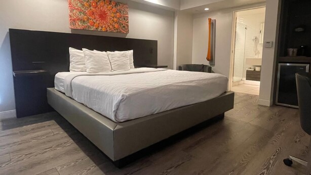 A modern bedroom with a large bed, a nightstand, a chair, and a bathroom visible through an open door. - Howard Johnson By Wyndham Tempe University/Phoenix (Tempe)
