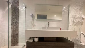 A modern bathroom with a glass-enclosed shower, a white sink with a dark wood vanity, and a large mirror above the sink. - Howard Johnson By Wyndham Tempe University/Phoenix (Tempe)