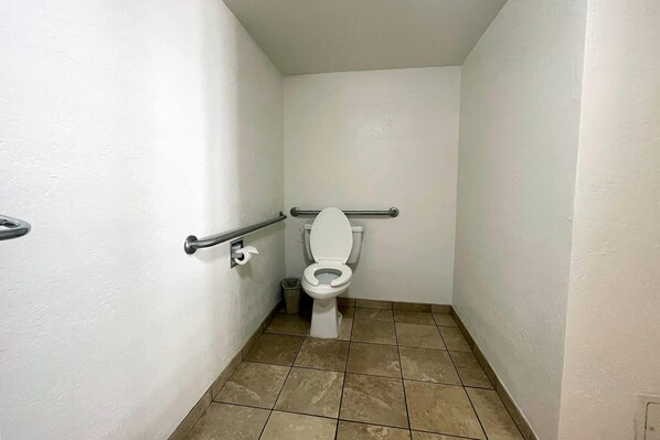 Ein kleines, schmales Badezimmer mit Toilette, Handlauf und Mülleimer.