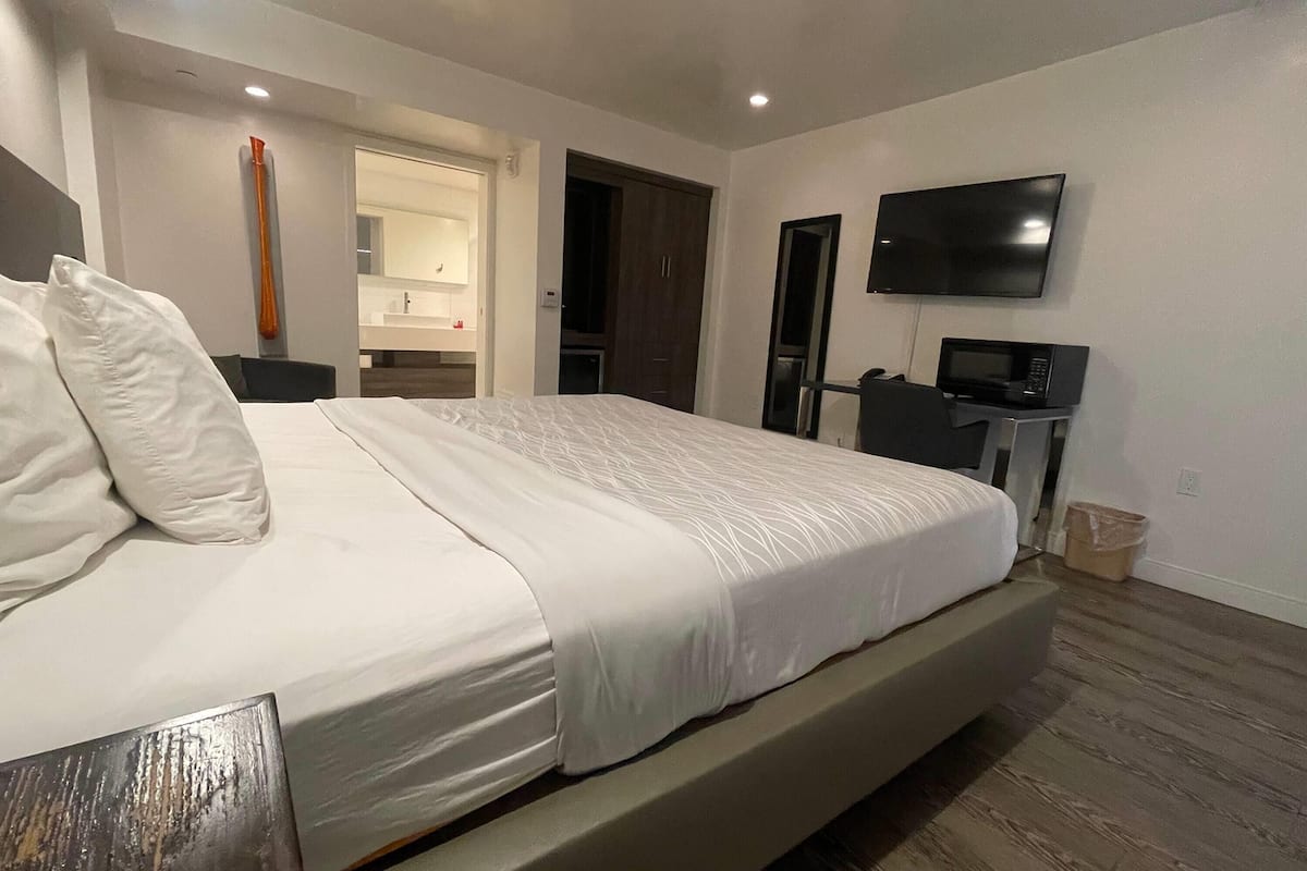 A modern bedroom with a large bed, a flat-screen TV, a microwave, and a bathroom visible through an open door.