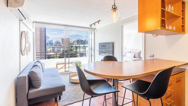 A modern living space with a dining area, a sofa, and a view of a cityscape through large windows. - Cozy 1-bedroom apartment in pleasant Providencia with AC (Providencia)