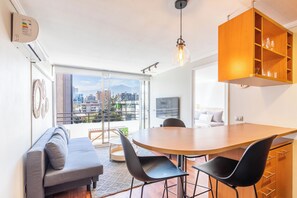 Un espace de vie moderne comprenant un coin repas, un canapé et une vue sur le paysage urbain grâce à de grandes fenêtres.