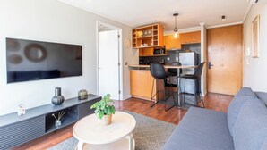 A modern living room with a flat-screen TV, a sofa, a coffee table, and a kitchen area with wooden cabinets and a microwave. - Cozy 1-bedroom apartment in pleasant Providencia with AC (Providencia)