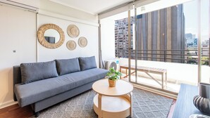 A modern living room with a grey sofa, a small round wooden table, and a balcony with a view of the city. - Cozy 1-bedroom apartment in pleasant Providencia with AC (Providencia)