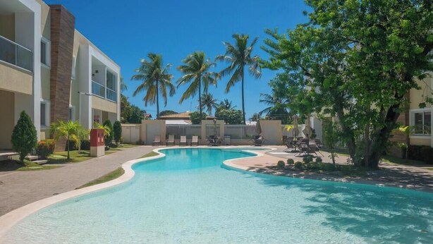 Une piscine à bord incurvé, entourée d’un sentier, de palmiers et d’un bâtiment doté d’un toit plat.