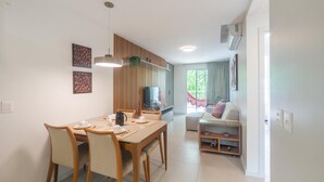 Un coin repas avec une table et des chaises en bois, un téléviseur et une cuisine en arrière-plan.