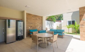 A modern kitchen with a refrigerator, a dining table with chairs, and a blue sofa. - Condo Apt w/ Pool in Guarajuba Agu0000 (Camaçari)