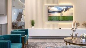 A modern living room with a large flat-screen TV mounted on the wall, a staircase leading to an upper level, teal upholstered chairs, and a decorative table with candles and a horse sculpture. - Dream 9BR Home - Game Room - Hot Tub - Sleeps 22! (Kissimmee)