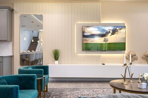 Ein modernes Wohnzimmer mit einem großen Flachbildfernseher an der Wand, einer Treppe zu einer oberen Ebene, honigfarbenen Polsterstühlen und einem Tisch mit Kerzen und einer Pferde Skulptur.
