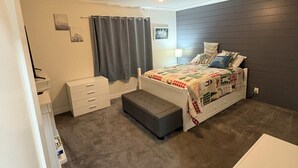 Un dormitorio con cama, mesita de noche, cómoda, ventilador de techo y ventana con cortinas.