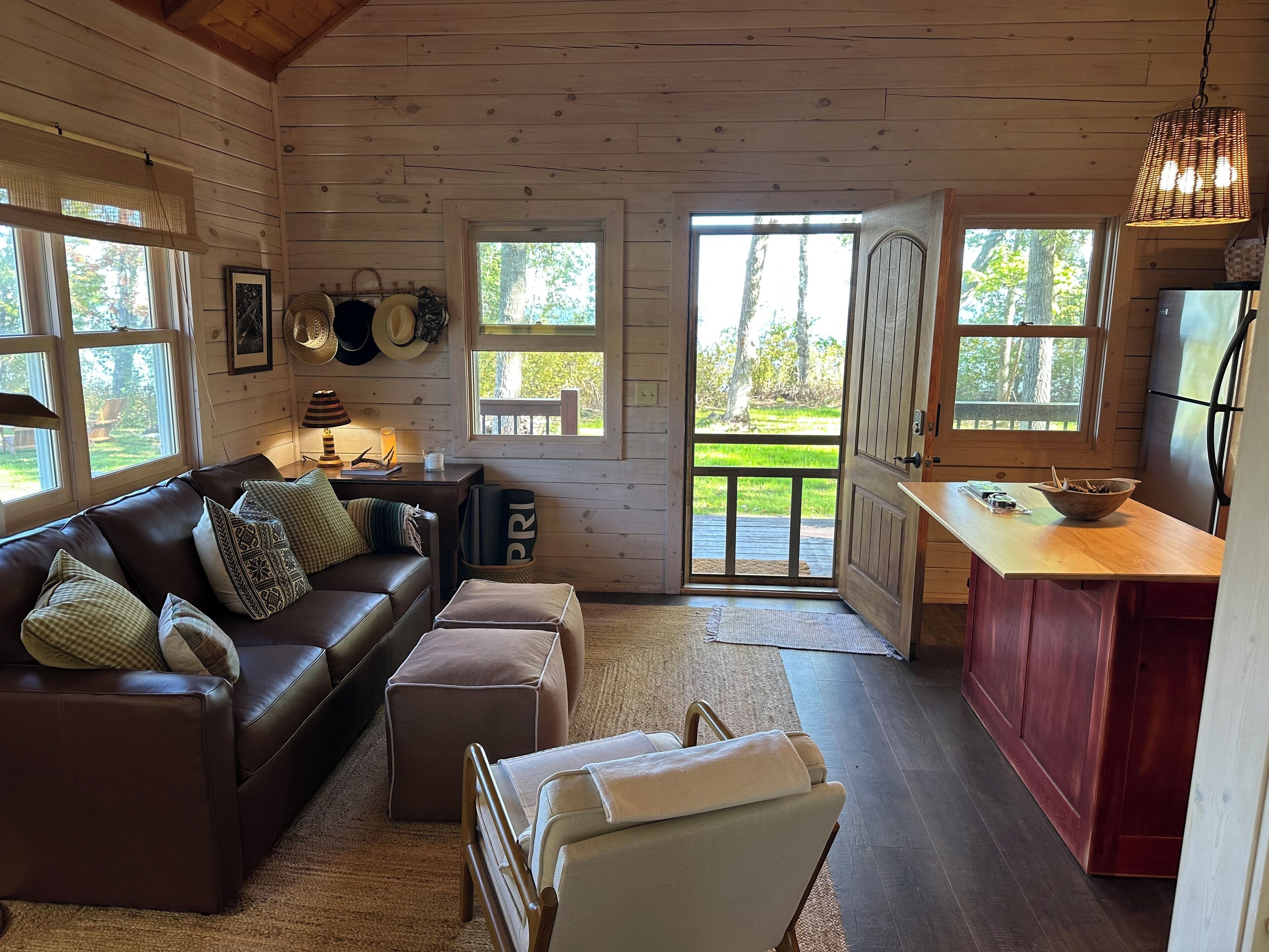 A cozy cabin interior with a leather sofa, a small table, and a kitchen area with wooden cabinets and a refrigerator.