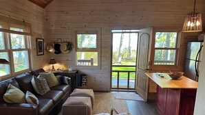 A cozy cabin interior with a leather sofa, a small table, and a kitchen area with wooden cabinets and a refrigerator. - Where wilderness meets luxury on Lake Winnie/Chippawa National Forest (Bena)
