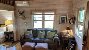 A cozy cabin interior with a leather sofa, two ottomans, a wooden ceiling, a mounted deer head, and a window with a view of the outdoors. - Where wilderness meets luxury on Lake Winnie/Chippawa National Forest (Bena)