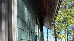 A green wooden house with a porch, a hose attached to the wall, and a view of trees and water in the background. - Where wilderness meets luxury on Lake Winnie/Chippawa National Forest (Bena)