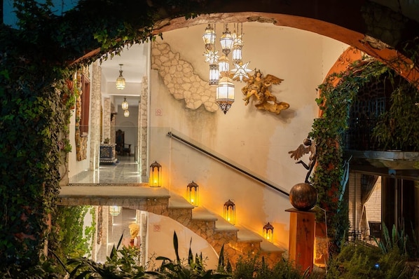 A staircase with lanterns, a stone wall with a star, and an archway with greenery. - Villa Peñasco (Ezequiel Montes)