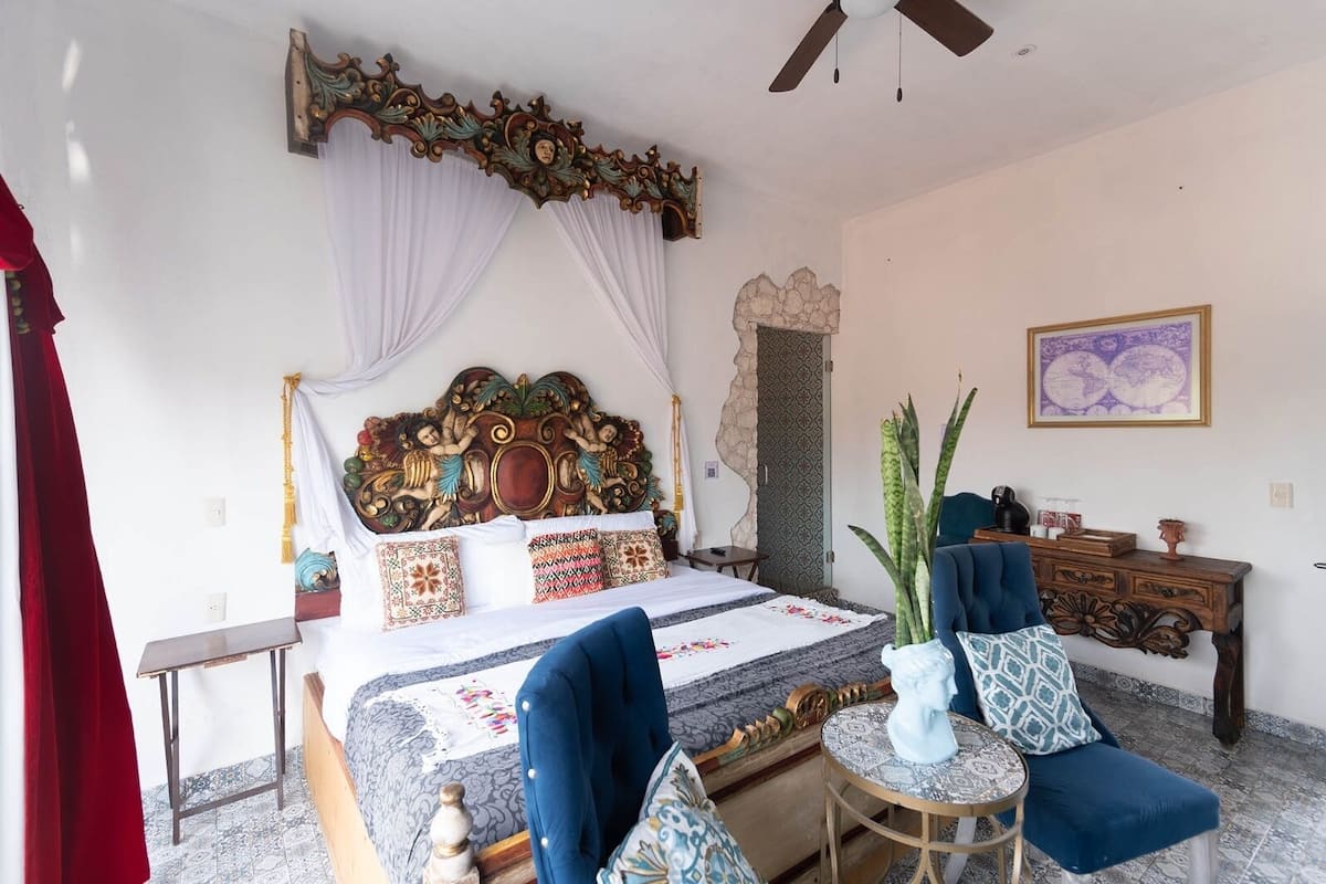 A bedroom with a large bed, a wooden headboard, a ceiling fan, a small table, and a chair.
