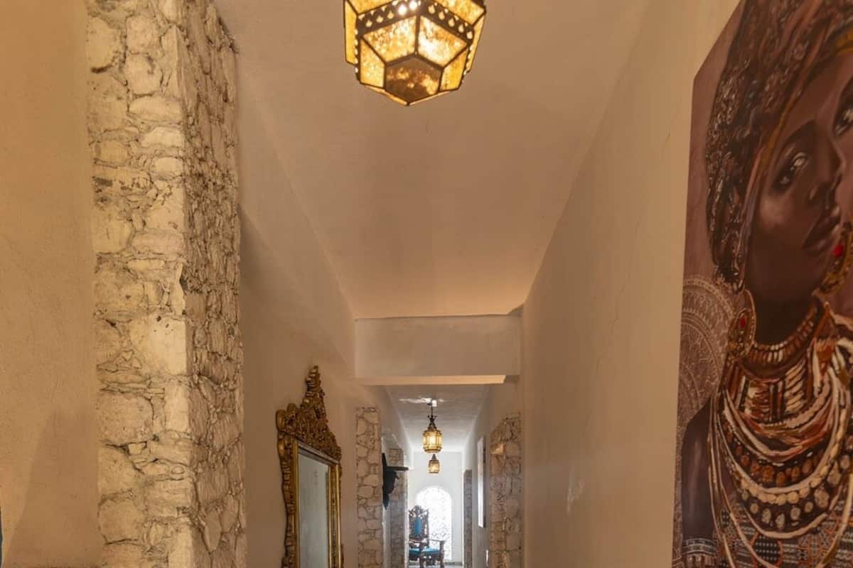 A hallway with patterned flooring, a stone wall, a decorative mirror, and a hanging light fixture.