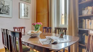 Ein Essbereich mit einem runden Tisch, Stühlen, einer Vase mit Blumen und einem Bücherregal im Hintergrund.