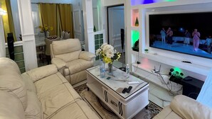 Una sala moderna con un sofá beige, una mesa de centro con un florero y un televisor de pantalla plana montado en la pared.