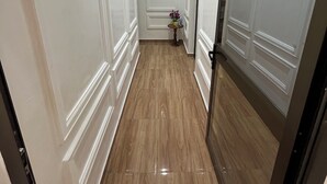 Un pasillo con paredes blancas y suelo de madera, que lleva a una puerta con un panel de vidrio.
