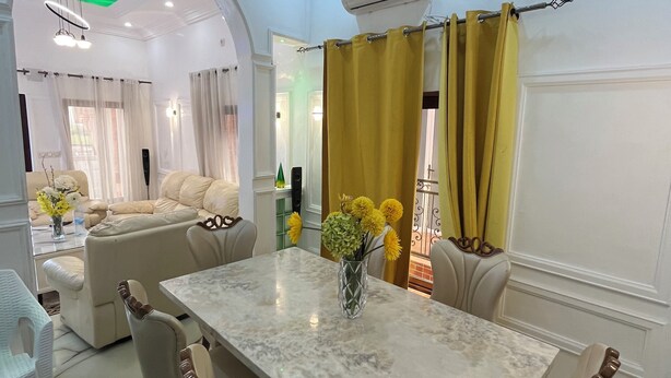 Un comedor con una mesa de mármol, sillas color beige y un jarrón con flores amarillas.