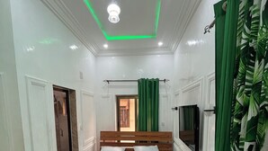 Un dormitorio con una cama de madera, paredes blancas, una cortina verde y una lámpara en el techo.
