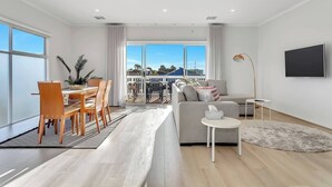 En moderne stue med spiseplads, store vinduer og en balkon.