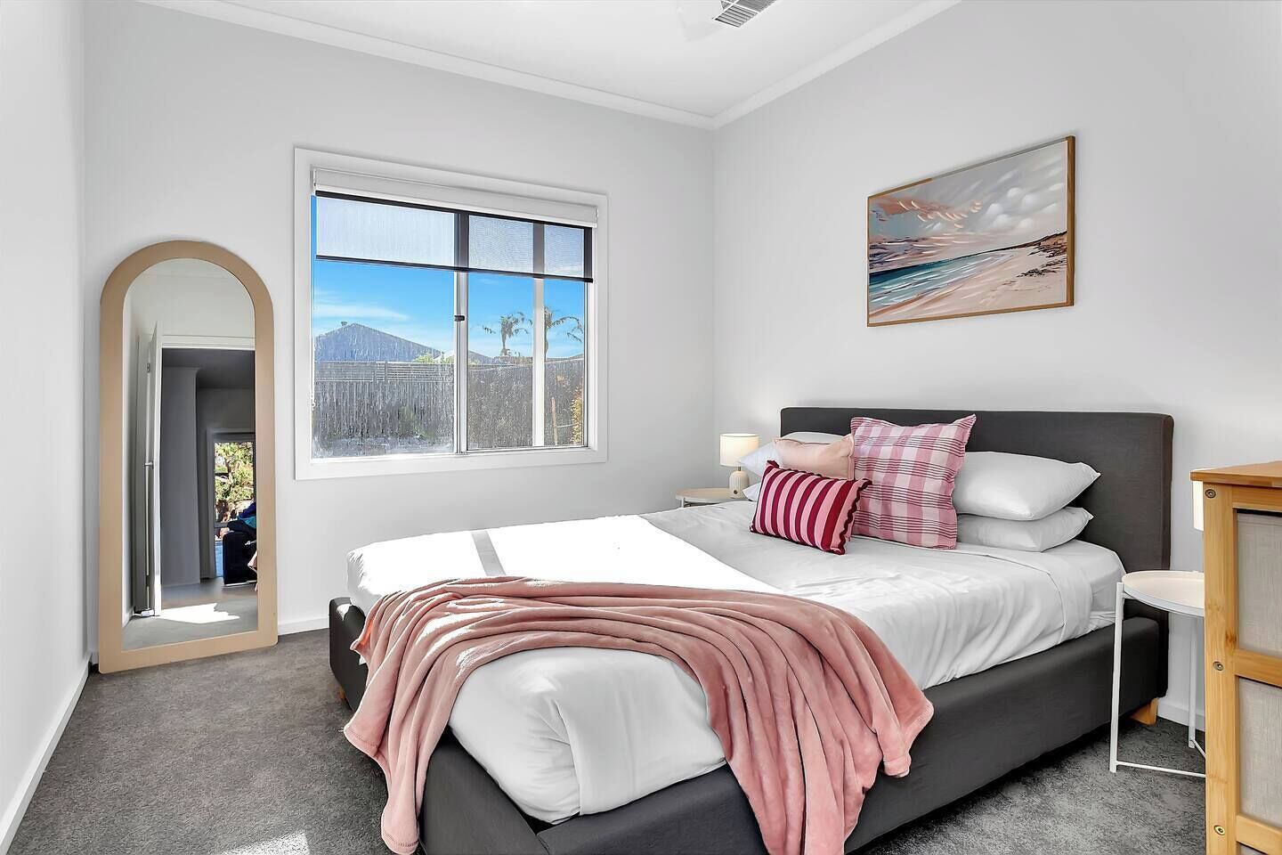 A modern bedroom with a large bed, a view of mountains through a window, and a painting on the wall.