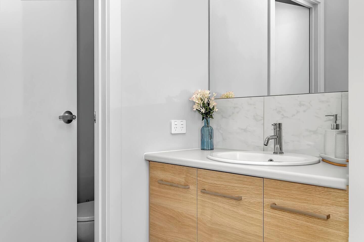 Een moderne badkamer met een witte wasbak, houten kastjes en een spiegel boven de wasbak.