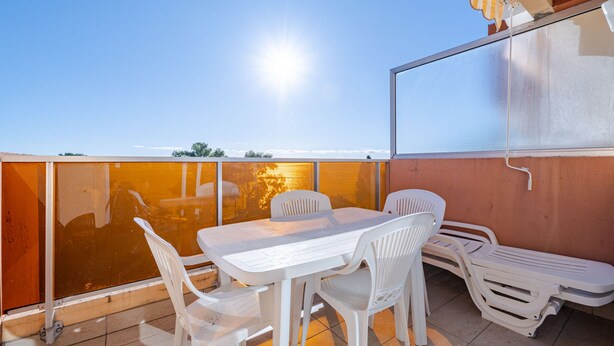 Un balcón con mesa y sillas, vista al atardecer y cielo despejado.