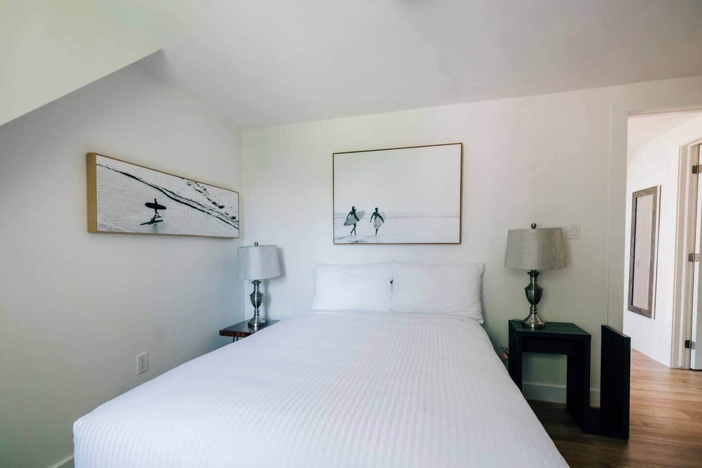A bedroom with a large bed, two bedside tables with lamps, and two wall-mounted paintings.