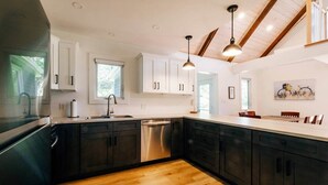A modern kitchen with dark cabinets, a stainless steel dishwasher, and a wooden countertop. - Forest Hills A-Frame (North Rustico)