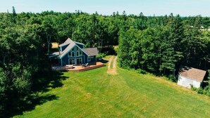 A large house with a spacious deck and a small shed in a forested area. - Forest Hills A-Frame (North Rustico)