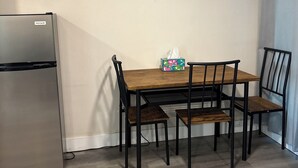 Een compacte keuken met een koelkast, een houten eettafel met vier stoelen, en een zakdoekendoosje op de tafel.