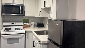 Een moderne keuken met witte kasten, een roestvrijstalen magnetron, gasfornuis en een zwarte koelkast.