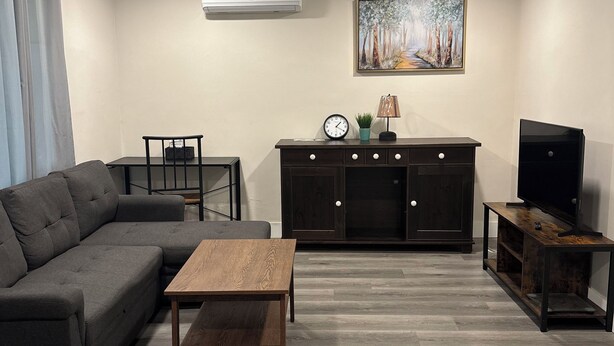 Een moderne woonkamer met een modulaire bank, een houten salontafel, een tv-meubel en een kast met een klok en een plant.