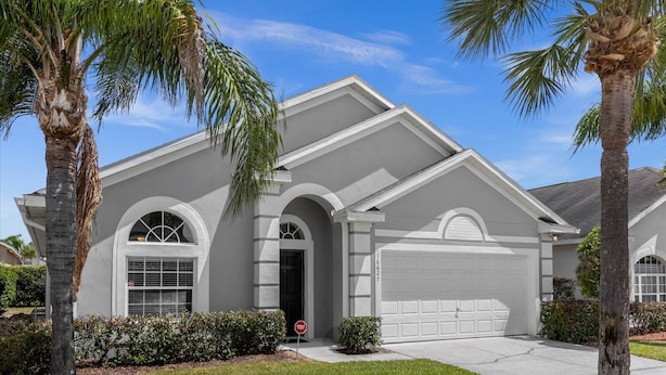 Una casa residenziale con garage, finestre ad arco e palme nel giardino.