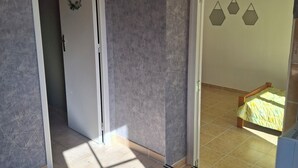 A room with a tiled floor, a bed with a yellow bedspread, a white door with a decorative emblem, and a wall with geometric patterns. - Maison du pecher 10 minutes from Beauval zoo (Couffy)