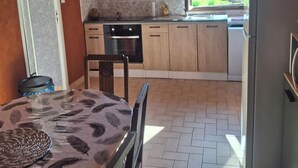 A kitchen with wooden cabinets, a dining table with chairs, and a view of greenery outside. - Maison du pecher 10 minutes from Beauval zoo (Couffy)