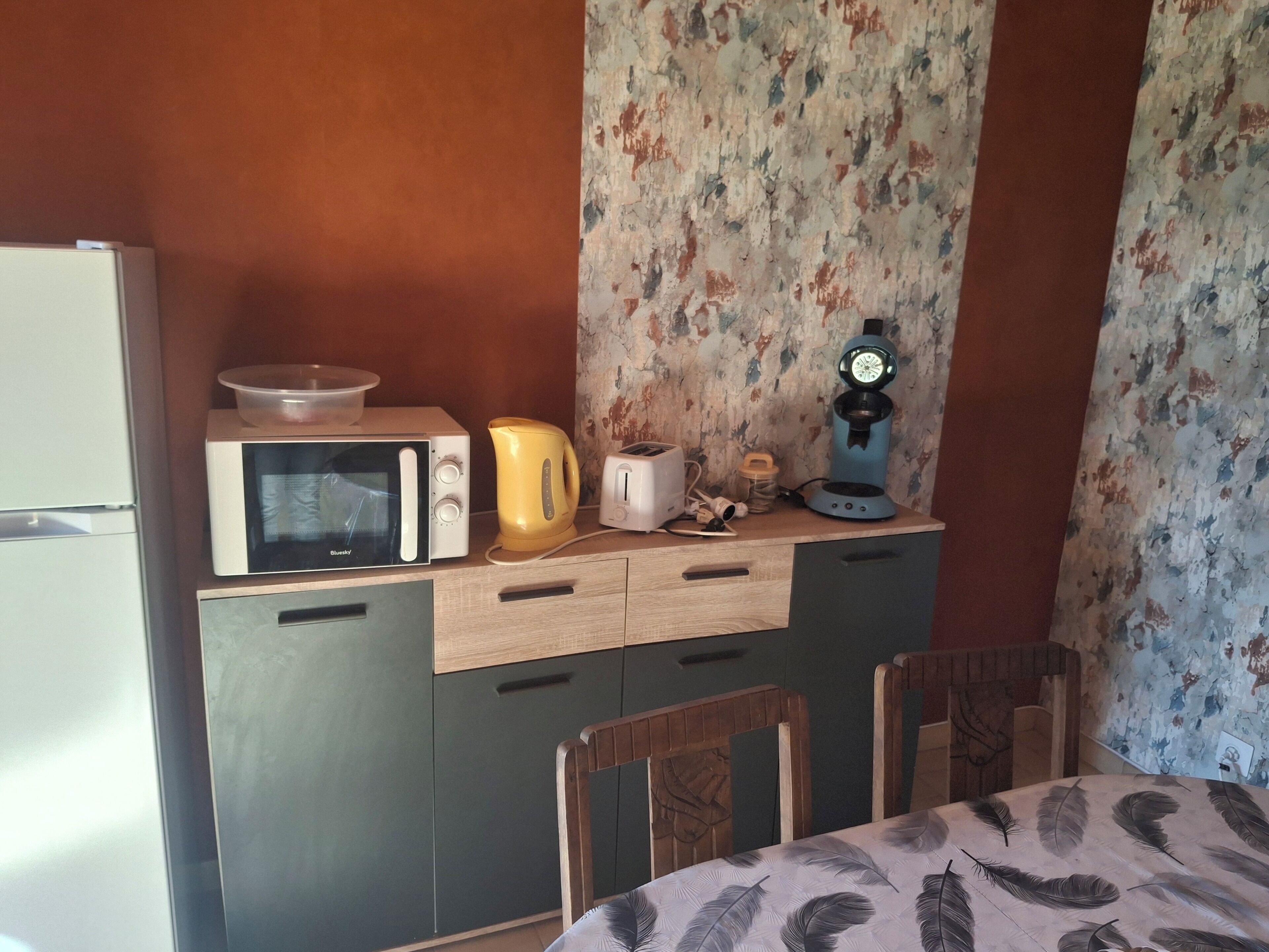 A compact kitchenette with a microwave, toaster, kettle, and coffee maker on a wooden countertop.