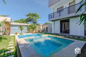 Ein modernes Wohnhaus mit Schwimmbad, überdachter Terrasse und einem zweistöckigen Gebäude mit Balkon.