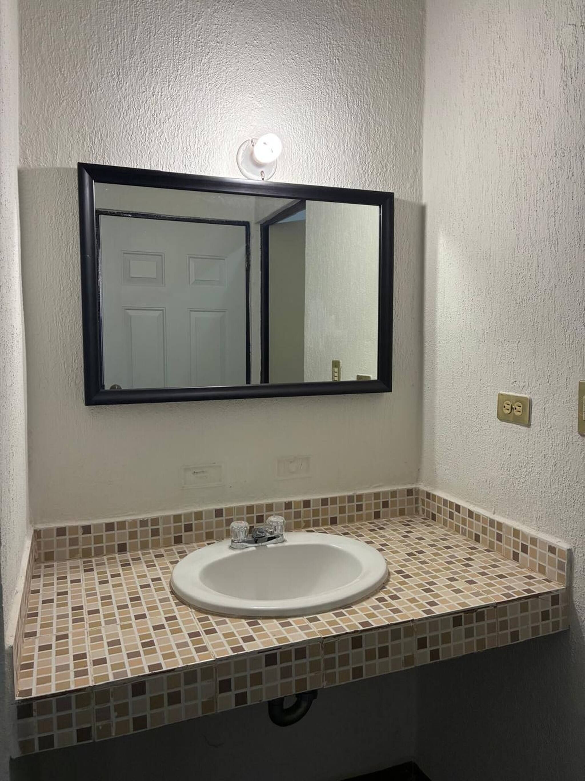 Un bagno con un lavandino bianco, uno specchio e uno schienale piastrellato.