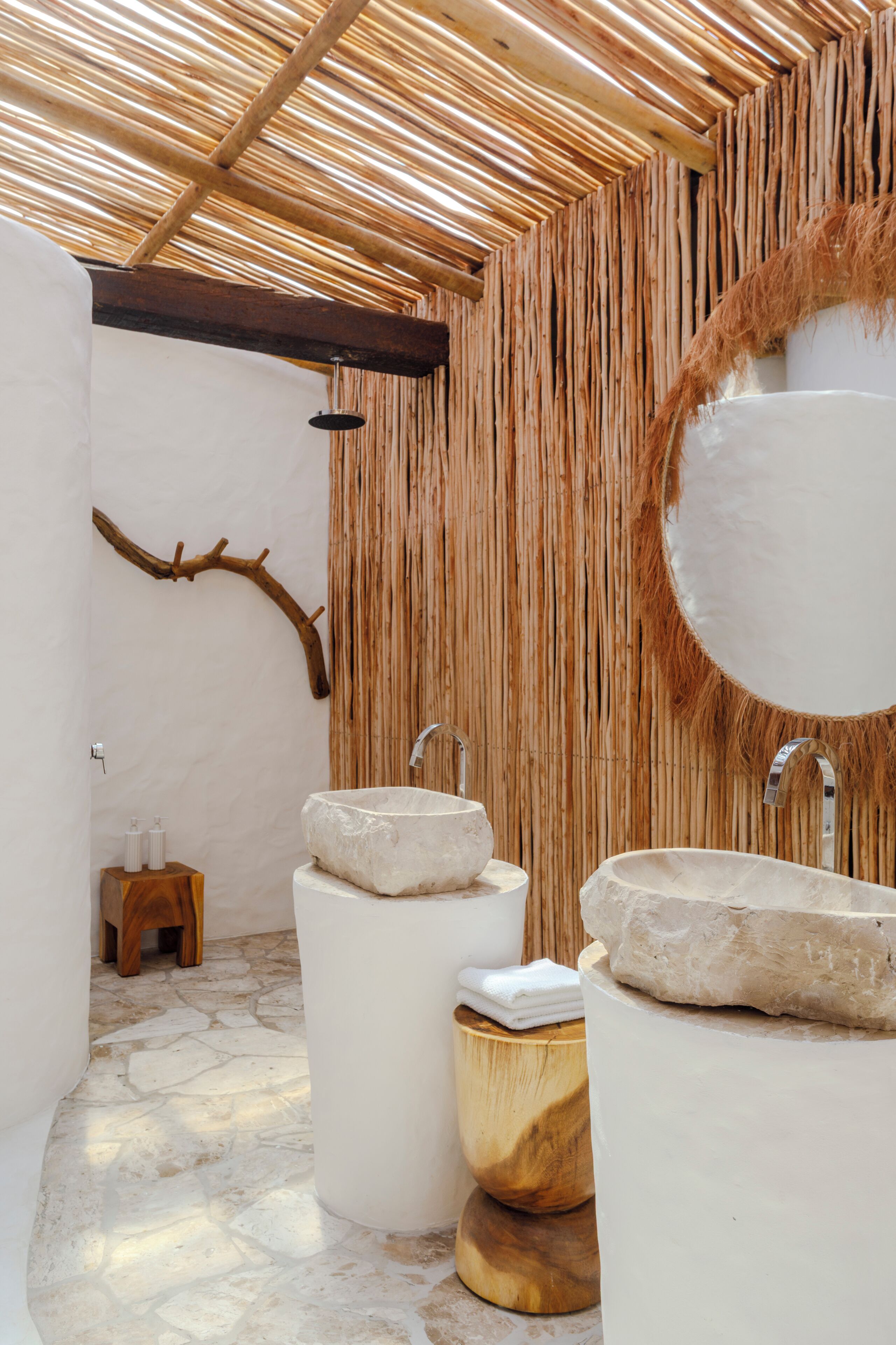 Une salle de bain avec deux vasques en pierre, un tabouret en bois et un mur recouvert d’un revêtement tissé.