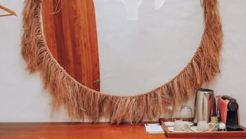Um espelho com moldura decorativa, uma porta de madeira, uma parede branca, um balcão de madeira, uma cafeteira, uma chaleira e uma pequena geladeira.